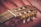 A close-up view of a classical guitar headstock displaying intricate tuning pegs and strings. The wood grain is visible, and the detail in the craftsmanship is highlighted against a soft, red background.