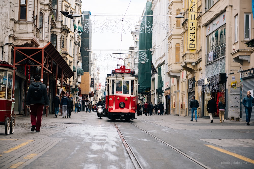 red tram near between buildings with person walking during daytime
