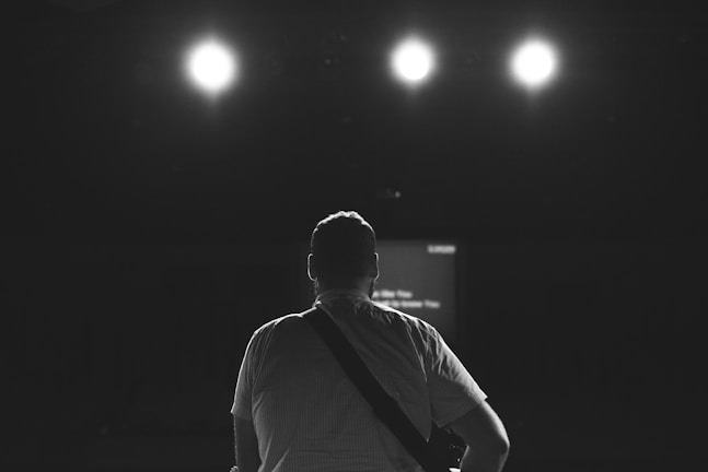 Silhouette of a musician holding an acoustic guitar on stage.