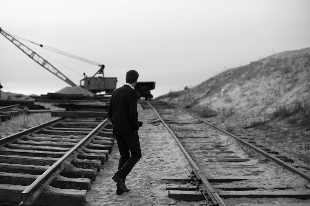 grayscale of man walking on train rail