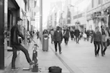 Black and white candid shot of a musician playing guitar on a city street.