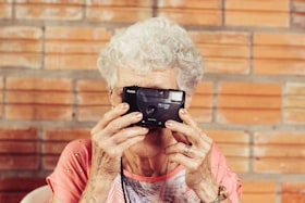 Mulher idosa segurando máquina fotográfica e observando pelas lentes da câmera 