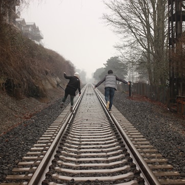 two person walking on the train rail