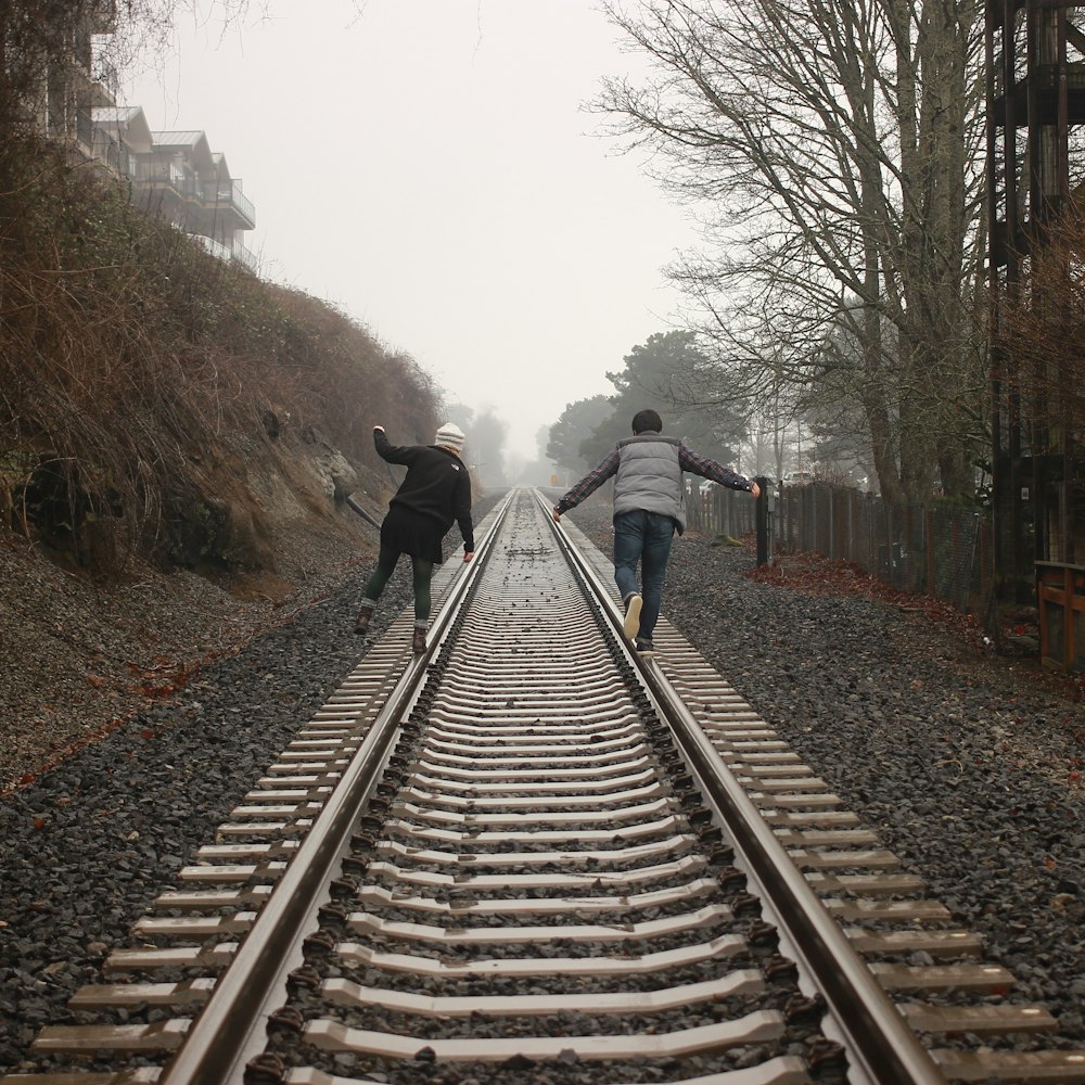 two person walking on the train rail