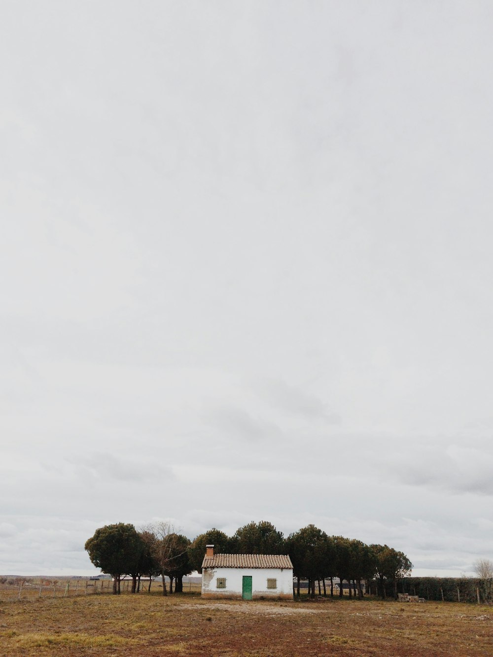 white house beside trees in front brown field