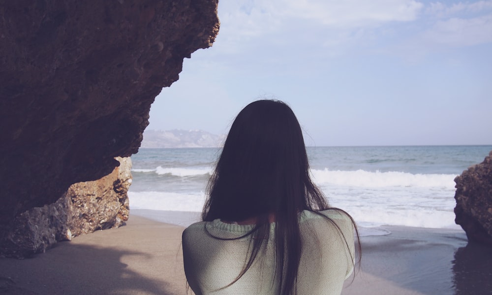 mulher sentada sob a rocha de frente para o mar