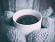 Close-up of a hand holding a cup of coffee wearing a knitted glove in warm tones