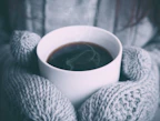 Close-up of a hand holding a cup of coffee wearing a knitted glove in warm tones