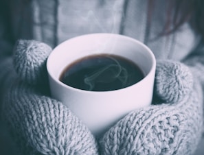 Hands in soft gloves holding a steaming cup of coffee during a winter commute