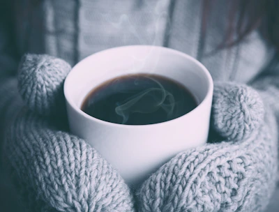 Close-up of hands holding a warm cup of herbal tea surrounded by cozy blankets.