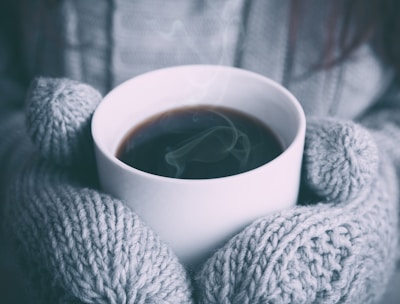Close-up of hands holding a steaming cup of herbal tea, resting on a cozy knitted blanket.