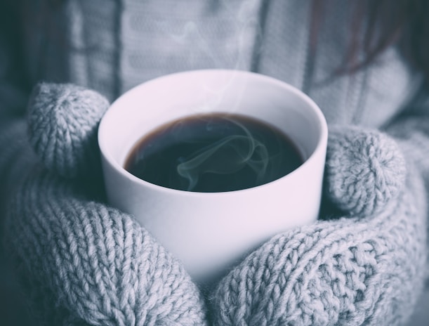 A cozy indoor scene with a pair of fleece-lined gloves resting on a wooden table next to a warm cup of tea.
