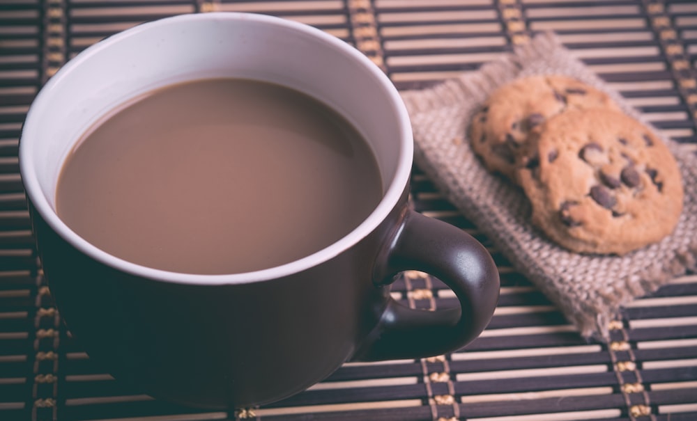 Xícara de cerâmica branca e marrom com café perto de biscoitos