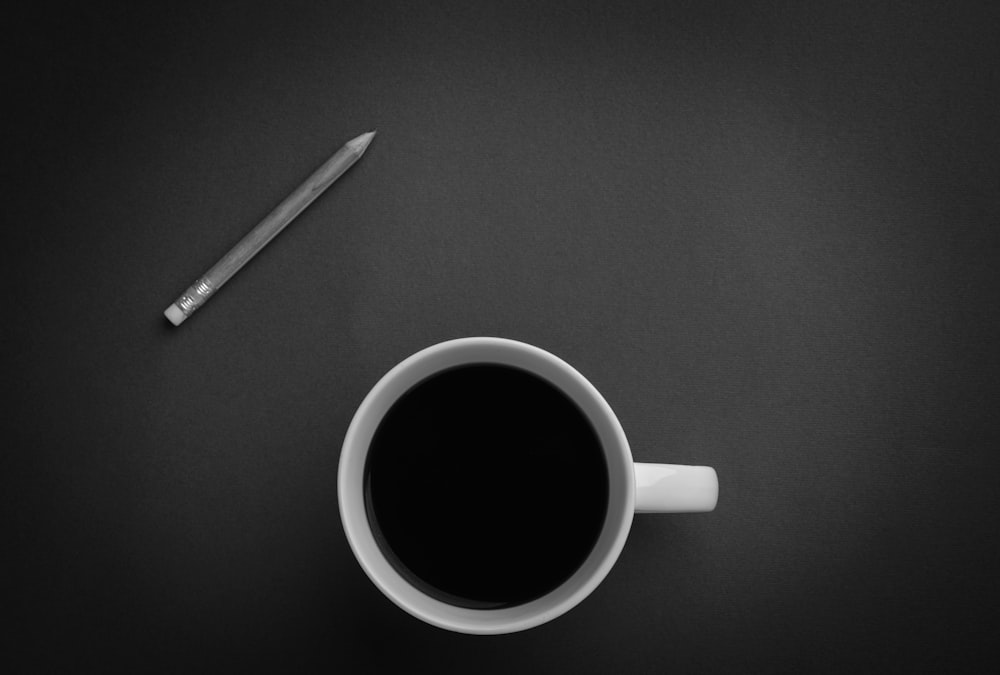 黒い表面に灰色の鉛筆の近くの白いセラミックのティーカップ