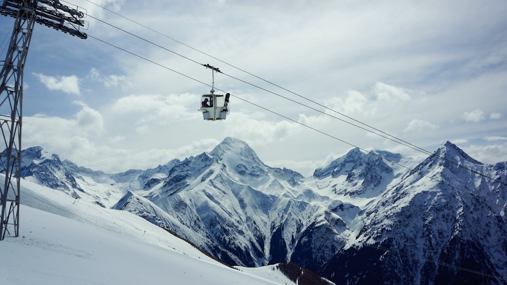 white cable car passing under snowfield during daytime