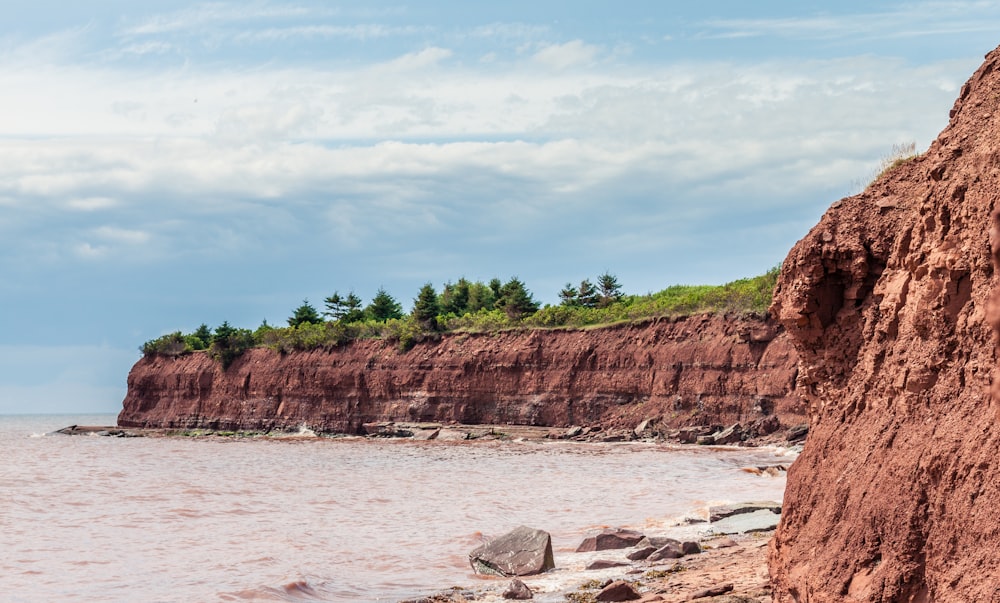 brown rocky mountain beside body of water during daytime