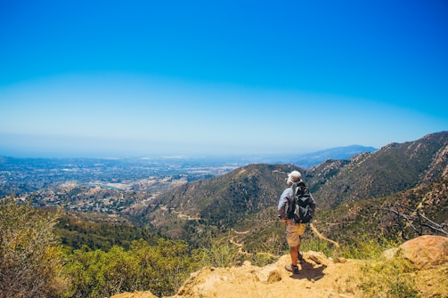 Hiker resting on a rocky outcrop overlooking a vast valley at dawn.