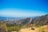 A hiker standing on a rocky outcrop overlooking misty hills under a bright blue sky.