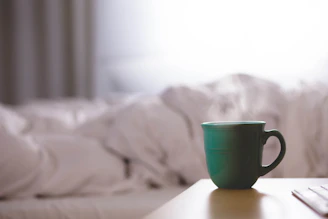 Close-up of a bright turquoise ceramic mug resting on a wooden table with sunlight streaming in.