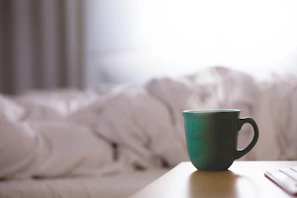Close-up of a bright coral mug resting on a wooden table with morning light casting soft shadows.
