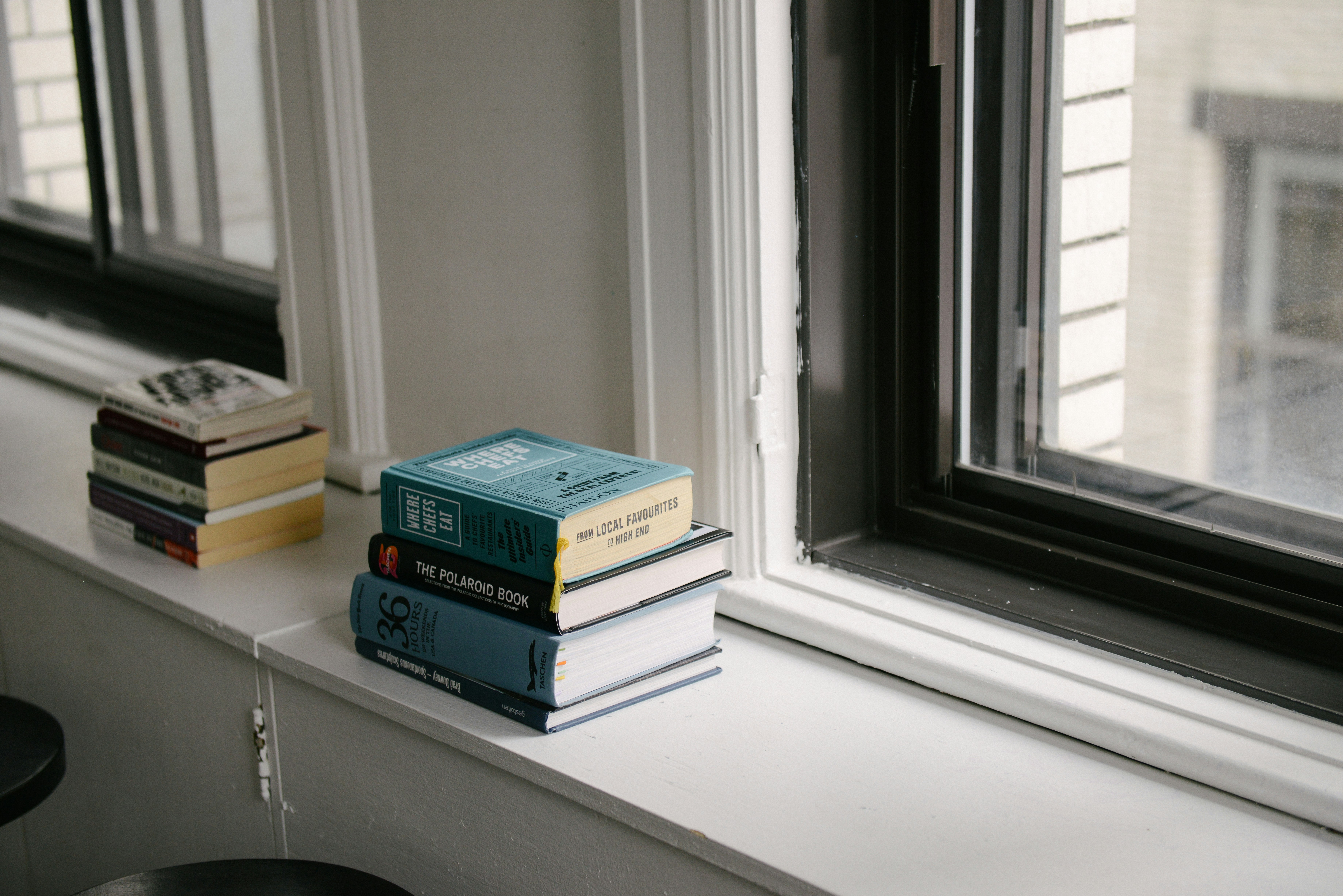 Two stacks of books on a window ledge