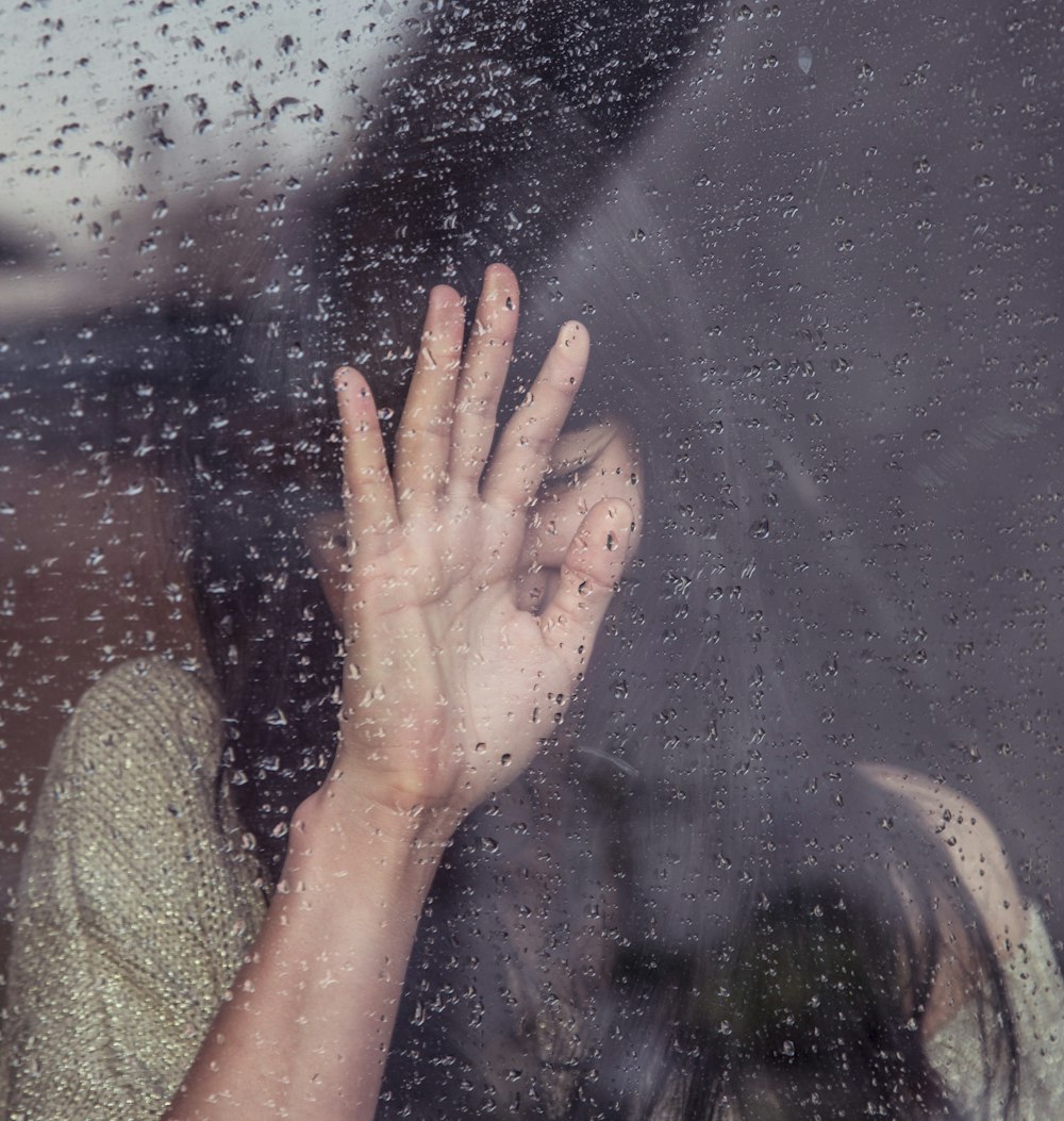 雨のガラスに触れる女性