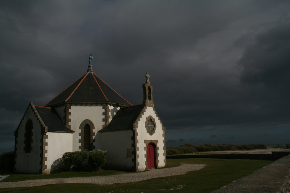 Chapelle blanche et grise entourée d’un champ d’herbe verte sous un ciel nuageux gris