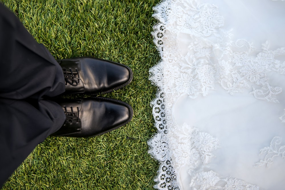 Bride wearing lace dress faces groom wearing black pants and shoes