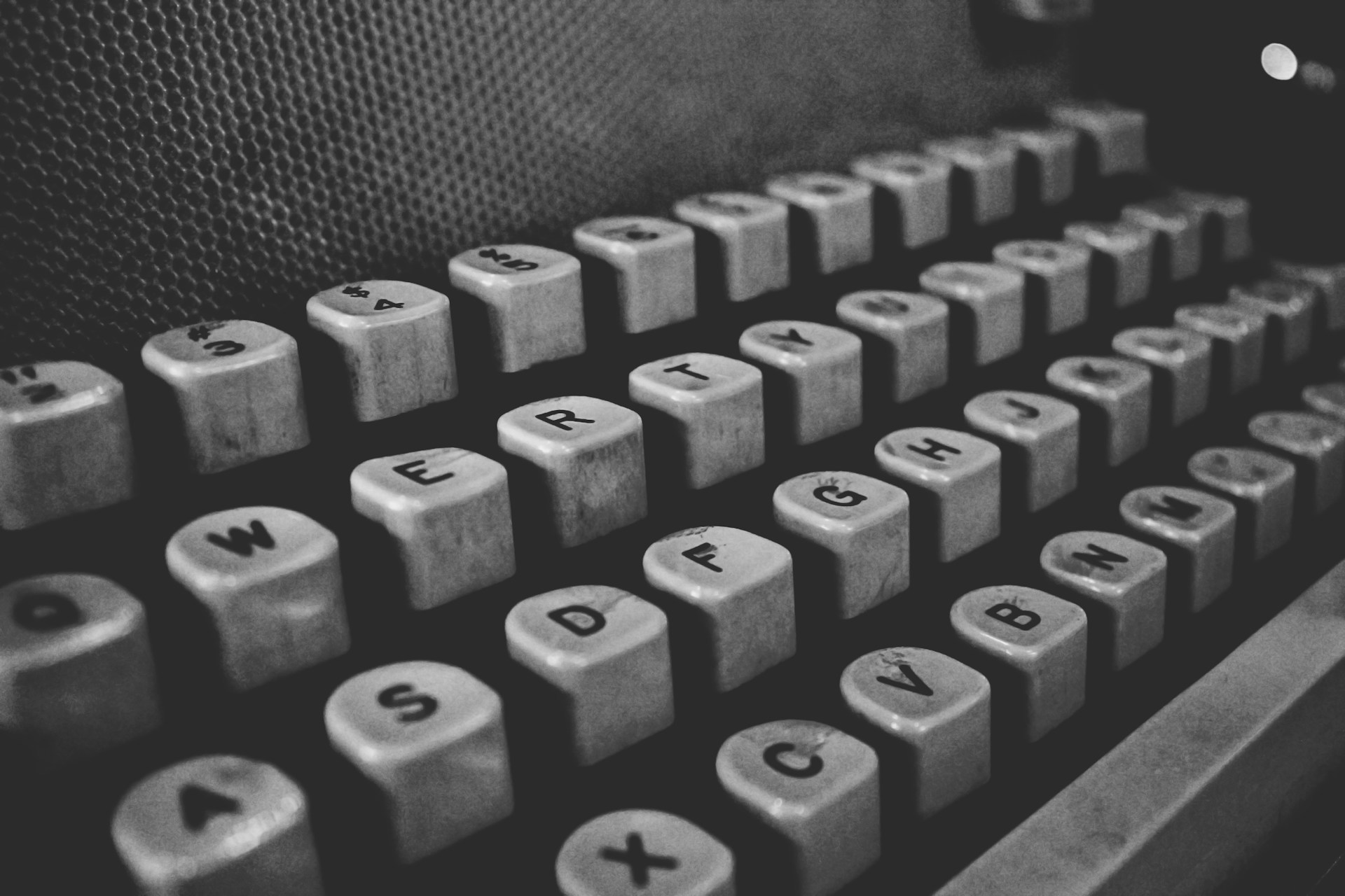 Black and white photograph of a vintage computer keyboard with stark shadows highlighting the worn keys.