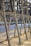 Metallic frame structure with rivets, positioned along a concrete waterfront. The blurred background features water and trees, hinting at an outdoor setting possibly along a river or canal.