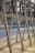 Metallic frame structure with rivets, positioned along a concrete waterfront. The blurred background features water and trees, hinting at an outdoor setting possibly along a river or canal.