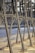 Metallic frame structure with rivets, positioned along a concrete waterfront. The blurred background features water and trees, hinting at an outdoor setting possibly along a river or canal.