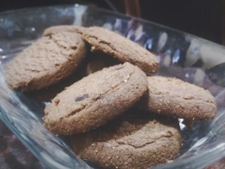 A glass bowl containing several brown cookies stacked on each other. The cookies appear freshly baked and have a coarse texture with visible chocolate pieces.