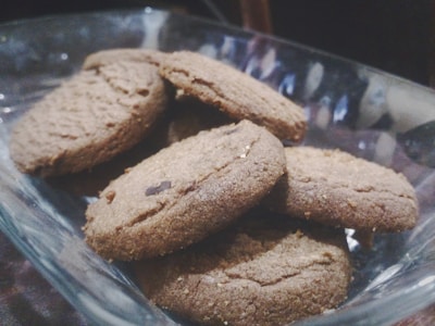 A glass bowl containing several brown cookies stacked on each other. The cookies appear freshly baked and have a coarse texture with visible chocolate pieces.