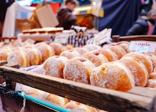 selective focus photography of doughnuts display on brown wooden trays near person wearing black hoodie