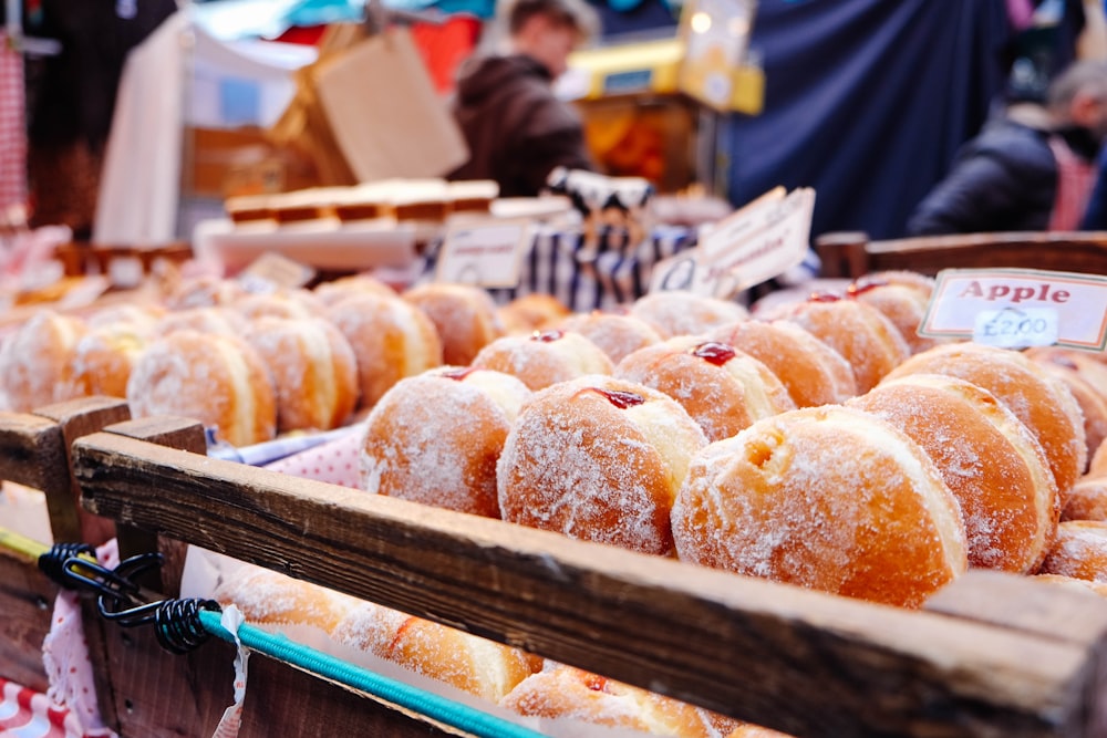 selective focus photography of doughnuts display on brown wooden trays near person wearing black hoodie