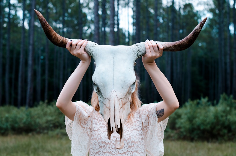 A woman in lace shirt holding up a bovine skull against a forest background
