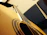 Close-up of a nylon-string acoustic guitar resting on a wooden chair next to a microphone.