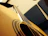 Close-up of a nylon-string acoustic guitar resting on a wooden chair next to a microphone.