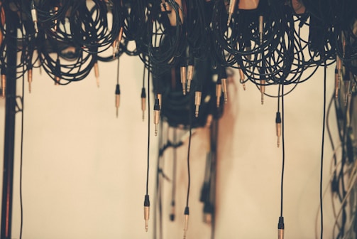 Various audio cables are hanging down, with a focus on numerous jack plugs extending from the coiled wires. The background is a soft, neutral tone, providing contrast to the dark cables.