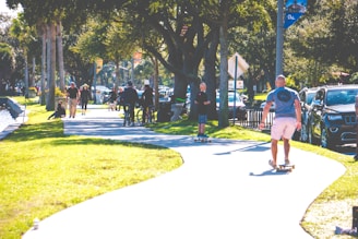 A diverse group of people in a park, some using wheelchairs and others walking, enjoying a sunny day together.