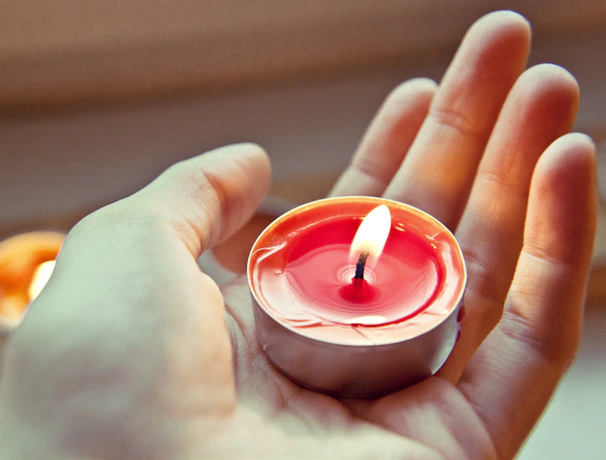 Close-up of hands holding a small devotional book with a soft glowing candle nearby