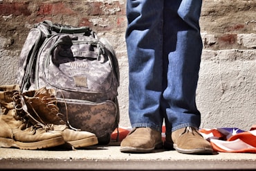 minimalist photography of person standing near backpack and boots