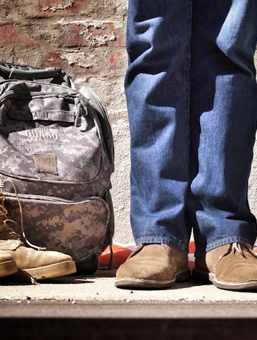 minimalist photography of person standing near backpack and boots