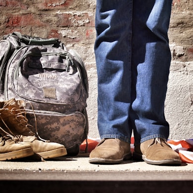 minimalist photography of person standing near backpack and boots