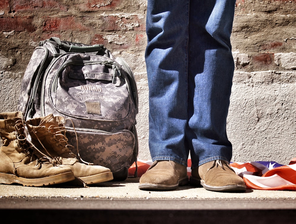 photographie minimaliste d’une personne debout près d’un sac à dos et de bottes