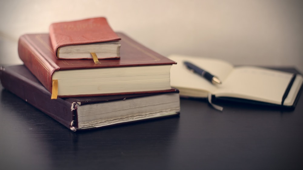 Fotografia de foco seletivo de três livros ao lado do caderno aberto