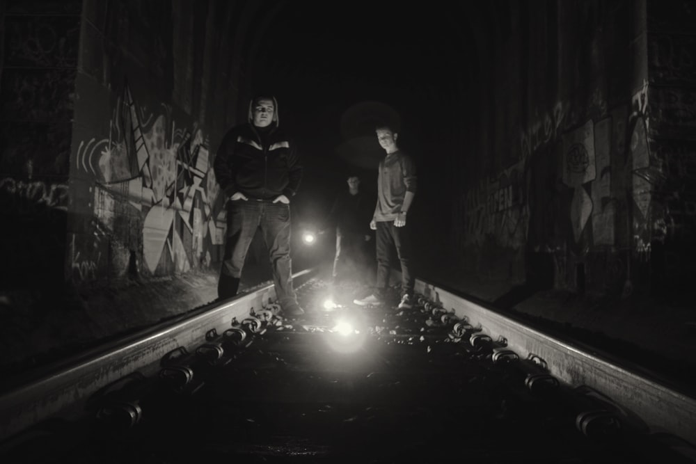 grayscale photography of two person standing on train rails