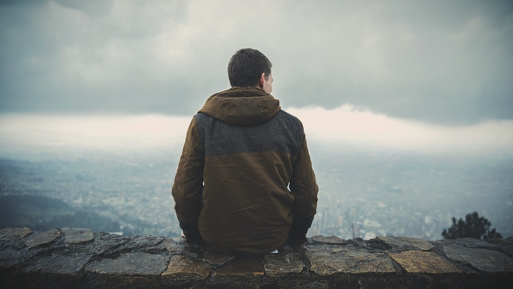 man sitting on brown concrete surface while staring sideway