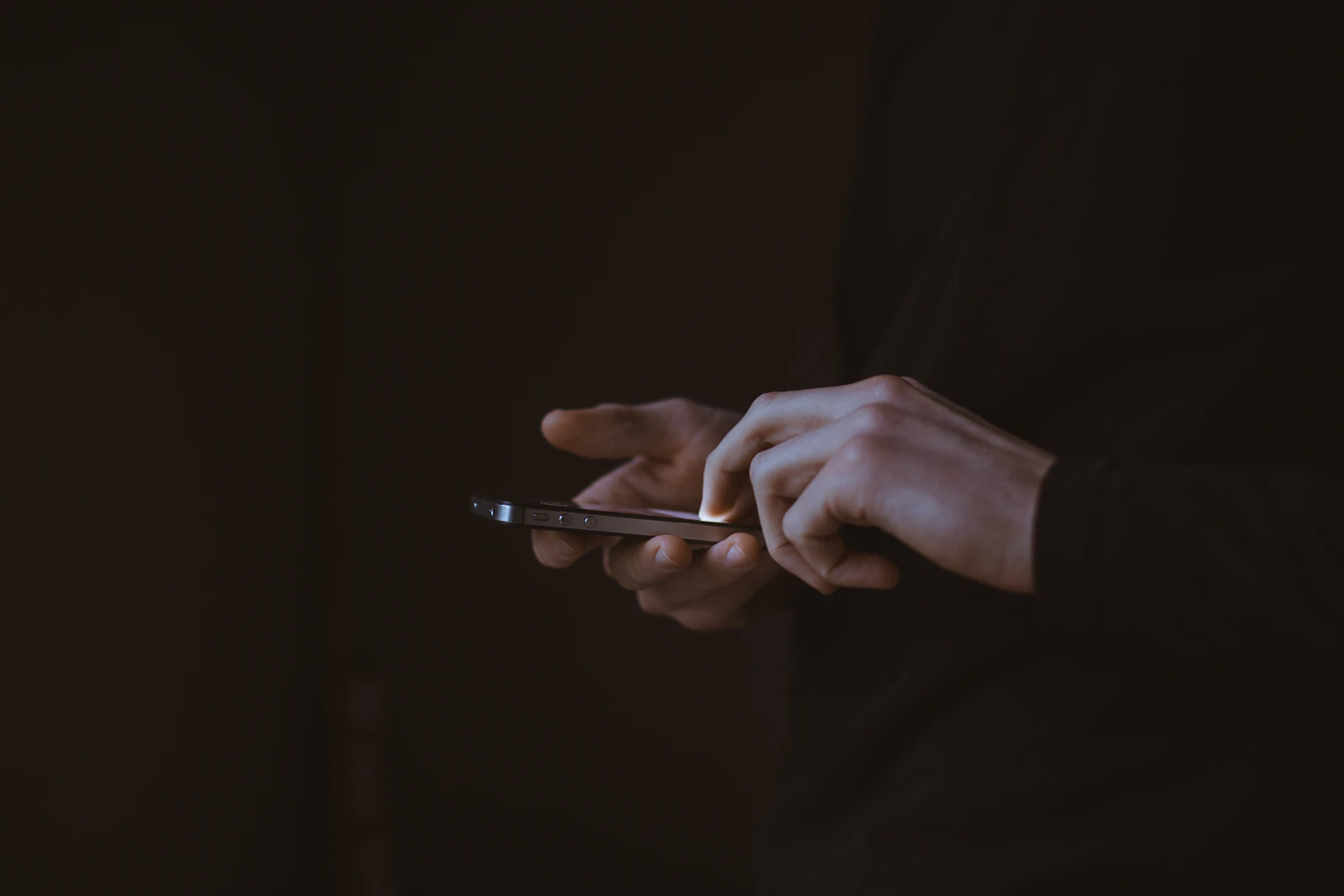 A silhouetted hand holding a smartphone in the dark